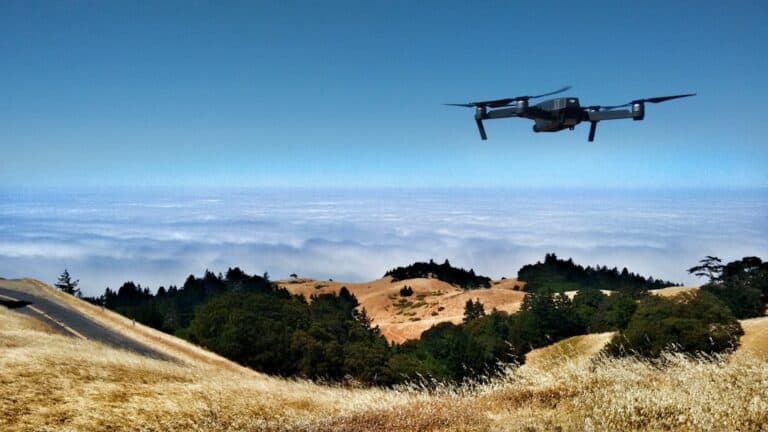 Drone flying over scenic, hilly landscape with cloudy backdrop.